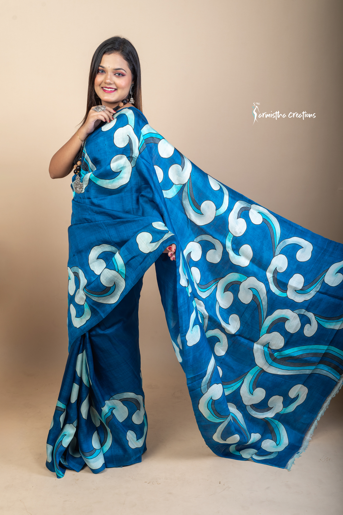 Bold and fluid like waves, this hand painted Bishnupuri silk saree features aqua and ivory motifs on an ocean blue base. Crafted from pure Bengal silk, it’s a lightweight, striking drape for standout moments.