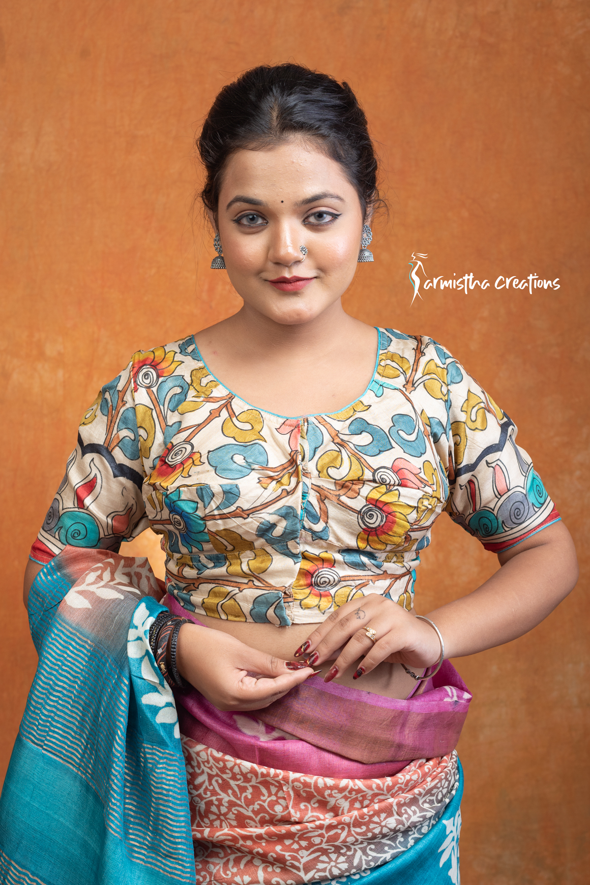 Charulata is a hand kalamkari ready-stitched blouse that embodies natural elegance. Featuring delicate floral vines and motifs in soothing tones of teal, mustard, and earthy hues on a cream base, this blouse carries the charm of handcrafted artistry.