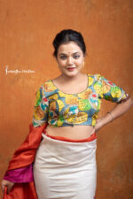 Kanakavalli is a hand kalamkari ready-stitched blouse inspired by the golden hues of autumn leaves. With bold leaf motifs in mustard, green, and teal against a bluish-grey base, this blouse celebrates nature’s seasonal beauty through artisanal craftsmanship.