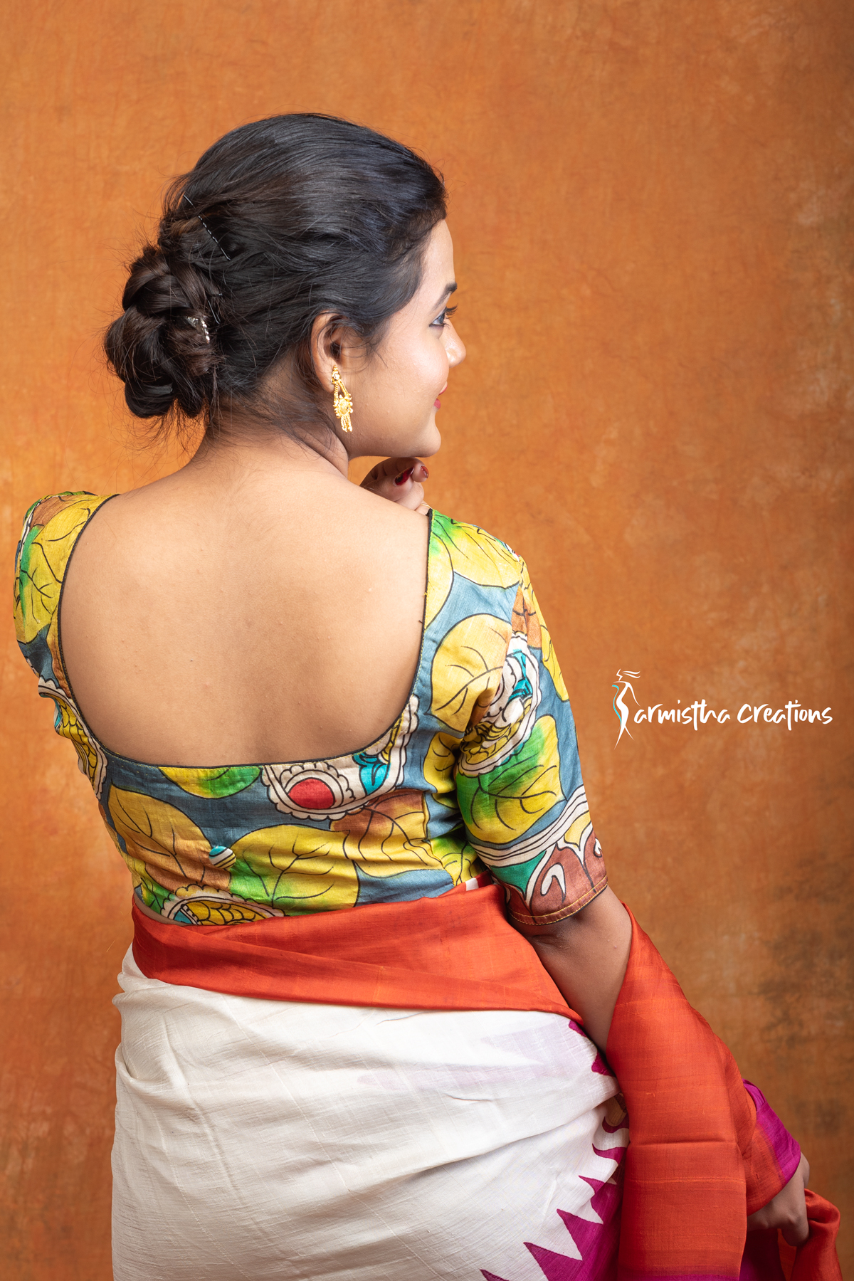 Kanakavalli is a hand kalamkari ready-stitched blouse inspired by the golden hues of autumn leaves. With bold leaf motifs in mustard, green, and teal against a bluish-grey base, this blouse celebrates nature’s seasonal beauty through artisanal craftsmanship.