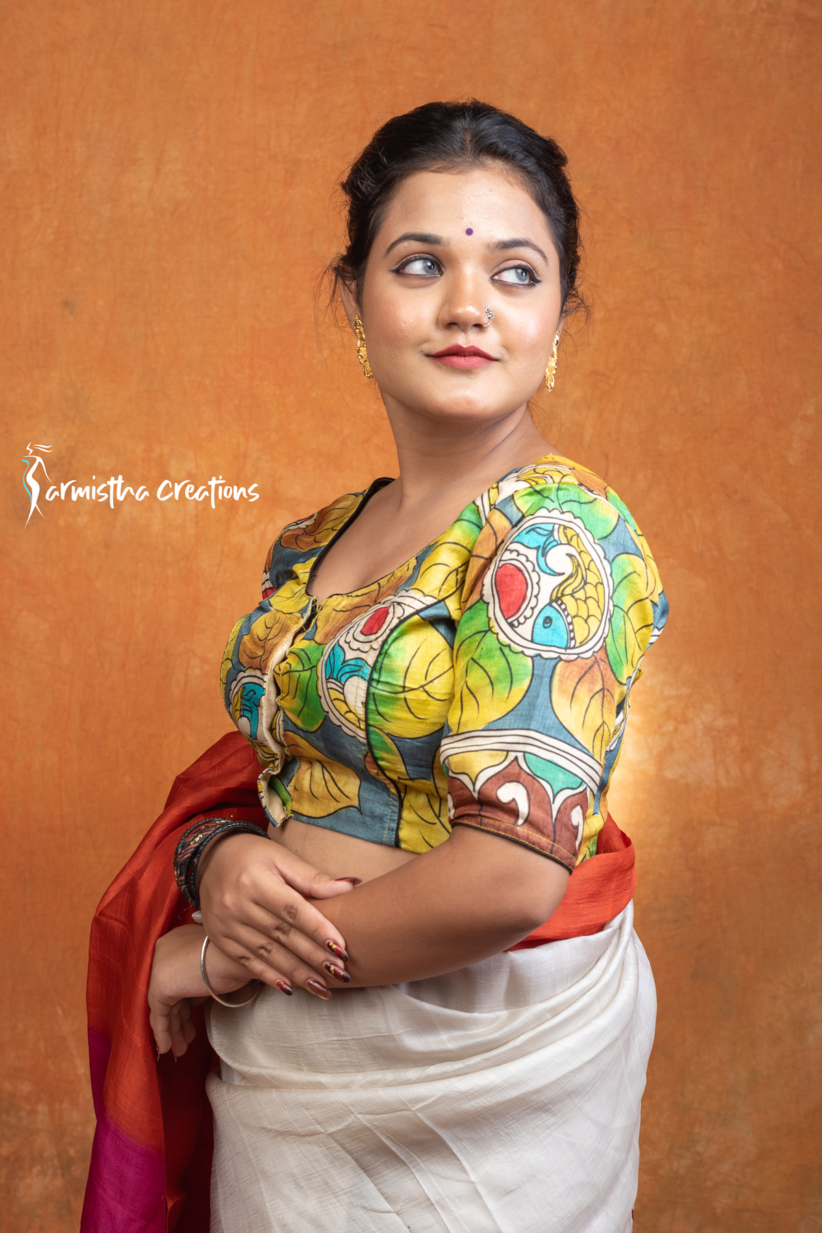 Kanakavalli is a hand kalamkari ready-stitched blouse inspired by the golden hues of autumn leaves. With bold leaf motifs in mustard, green, and teal against a bluish-grey base, this blouse celebrates nature’s seasonal beauty through artisanal craftsmanship.