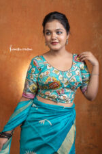 Tarangini is a hand kalamkari ready-stitched blouse that mirrors the grace of flowing waves and blossoming gardens. Set against an aqua-blue base, the blouse features intricate floral vines in coral, mustard, and green, evoking freshness and vibrance.